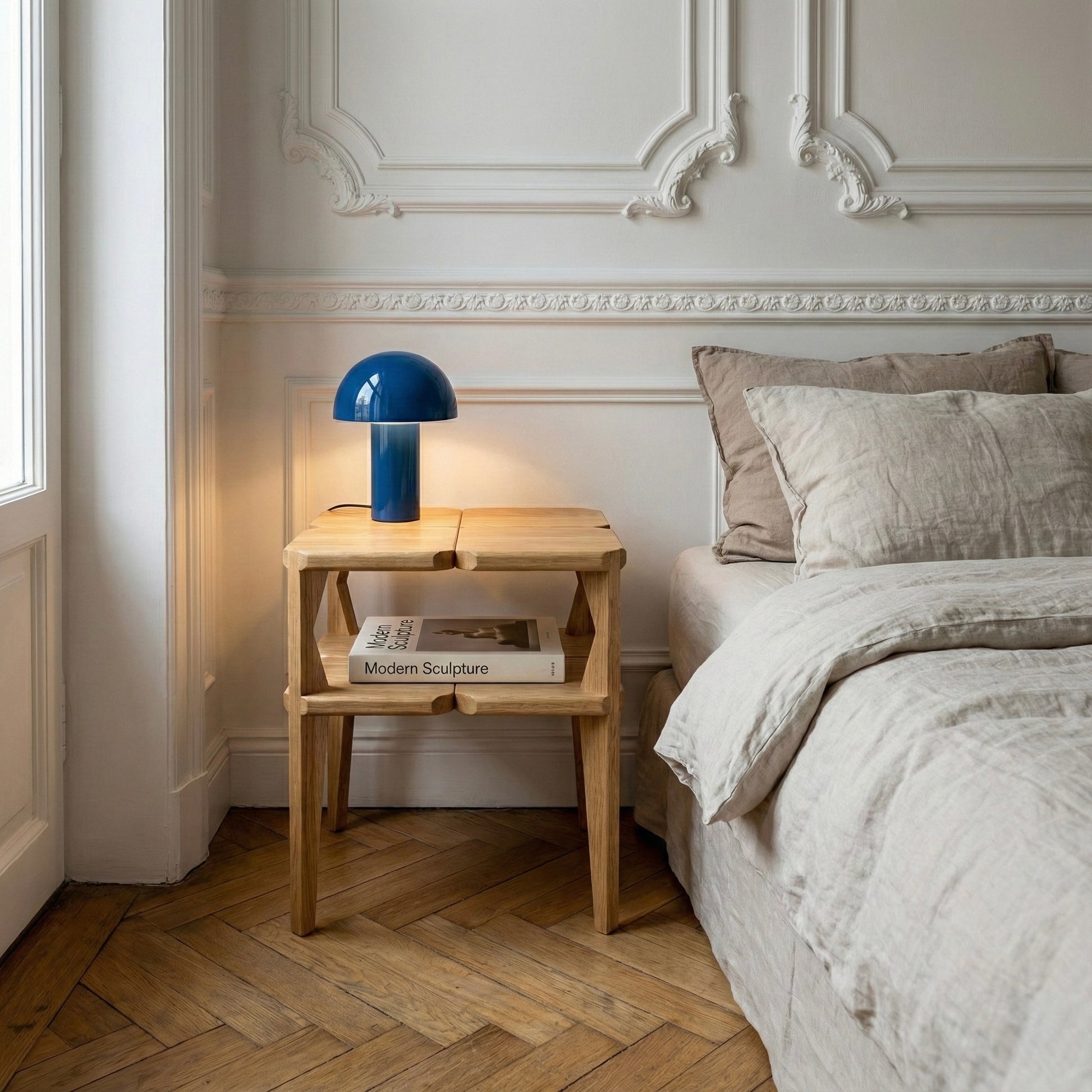 Neatly made bed with wooden side table and blue lamp in a bedroom setting.